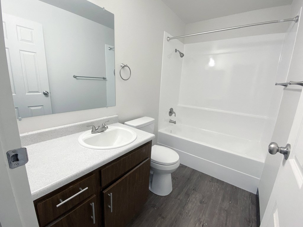 Full bathroom with wood-like flooring, vanity sink, large mirror, toilet, shower, and towel rack.at Laurel Park, Twin Falls, ID