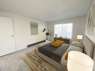 Bedroom with white walls, oversized window with natural light, gray carpet, staged with bed, side tables, dresser, and plant.at Laurel Park, Twin Falls, 83301