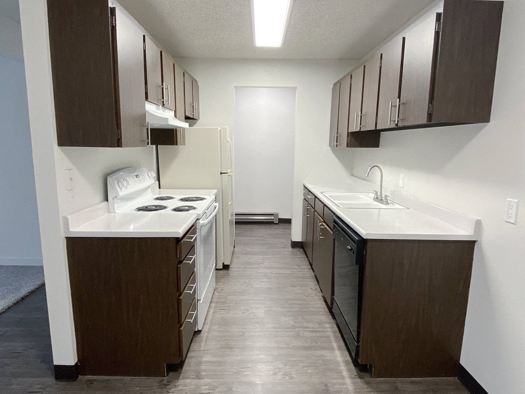Double galley kitchen with wood-like flooring, white counters, appliances, and top and bottom cabinet storage.at Laurel Park, Idaho
