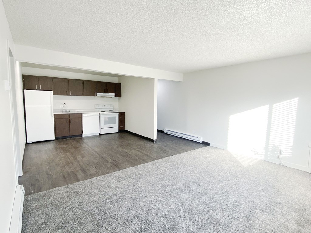 Open living room looking into dining area and galley kitchen with wall dividing hallway. White appliances, cabinet storage.at Laurel Park, Twin Falls, 83301