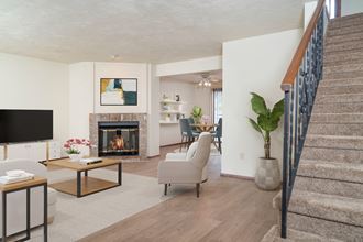 Oversized living room with brick fireplace in the center, staged with couch, chair, media console, TV, and plant.