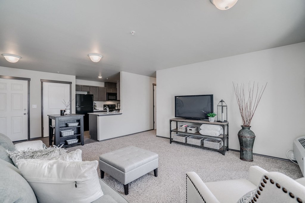 Large carpeted living showing a chair, couch, tv and plant. Open floor plan from dining room and kitchen. Hallway off of living to bedrooms. at Altitude, East Wenatchee, WA