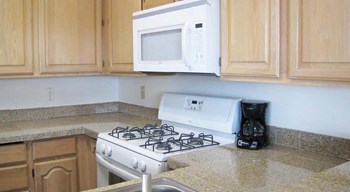 Kitchen with upper and lower cabinets, and white microwave and oven with stove cooktop. - Photo Gallery 3