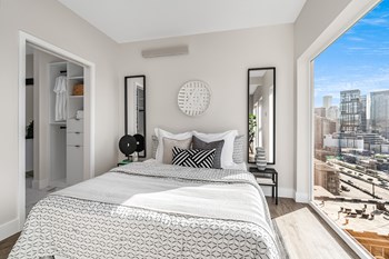 Bedroom with floor-to-ceiling window and city views opposite the walk-in closet. Staged with a bed, side tables, and mirrors. - Photo Gallery 10