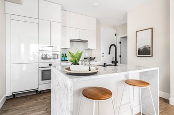 Bright modern kitchen with sink, oven, flat stovetop, microwave, and a waterfall island staged with barstool chairs. - Photo Gallery 8