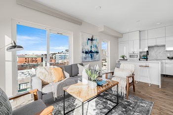 Living room with wood-style flooring, looking into kitchen, floor-to-ceiling window, and sliding door, city views. - Photo Gallery 7