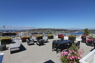 Rooftop deck with patio tables and chairs, planted boxes with flowers, and views of Elliot Bay, Lake Union, and Space Needle.