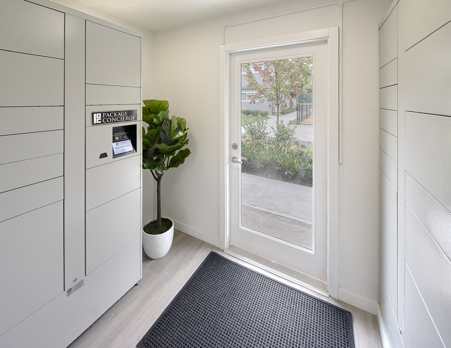 Secure package concierge system indoors by exterior door. Area contains a plant and rug. at 3030 Lake City, Seattle