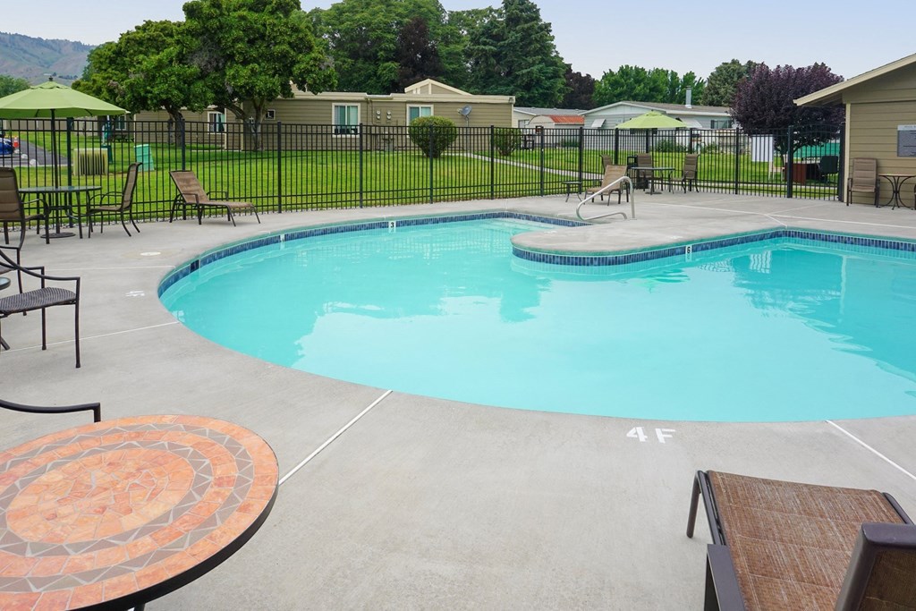 Curved outdoor pool with chairs and tables and a fence around it.at Park View Apartments, Wenatchee, WA 98801
