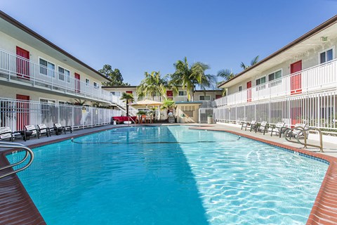 Outdoor swimming pool with sun chairs, a lounge area lined with apartments, and palm trees at Pacific Sands, San Diego, CA