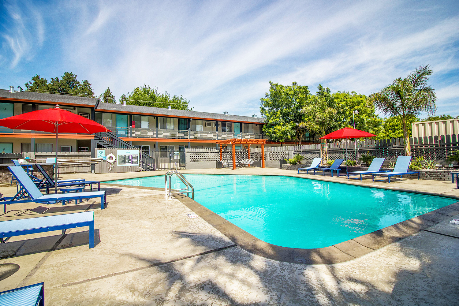 Woodland Village pool with blue lounge chairs, red umbrellas and landscaping.at Woodland Village Apartments , Woodland