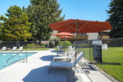 Community pool with lounge chairs and orange umbrellas surrounded by grass at Castlerock, Wenatchee