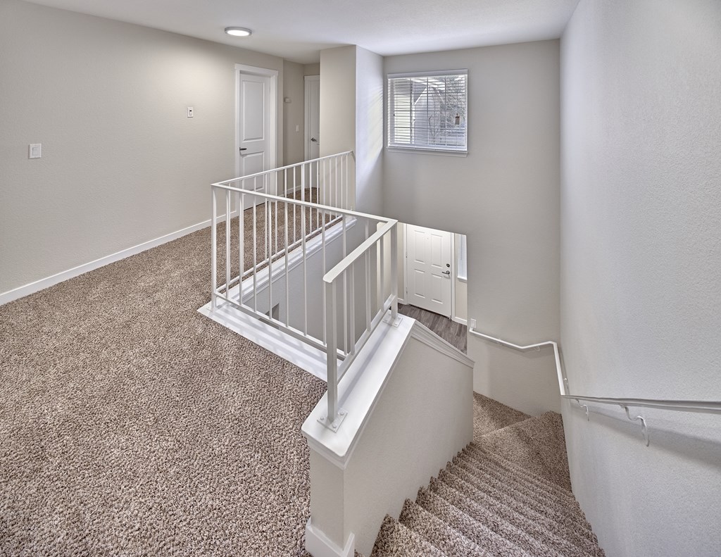 Carpeted stairs with white railings look down to the first floor. Above the stairs is a large window at Arterra Apartments, Washington