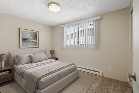 Carpeted bedroom with queen bed and large window with blinds for natural light at the Lakes Apartments in Moses Lake