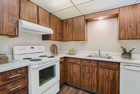 Kitchen with warm wood cabinets, white electric range, and ample counter space at The Lakes Apartments