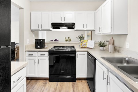 A black dishwasher is in the middle of a white kitchen.