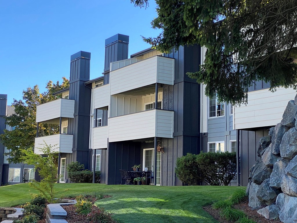Apartments with balconies and patios are surrounded by manicured grass, landscaping, and trees at University Glen, University Place, WA, 98466