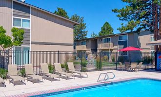 Swimming pool with sun chairs, umbrella-covered seating, surrounded by a fence, apartments, and landscaping.at Wildflower, Kennewick, WA