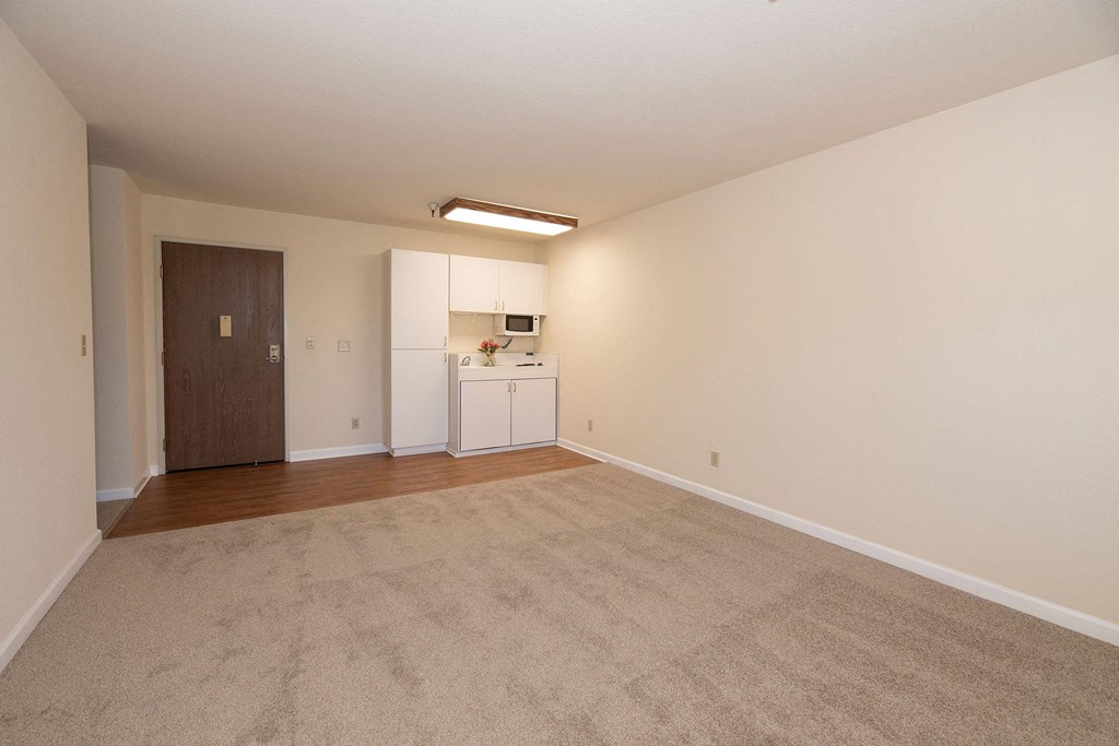 an empty living room with a kitchen in the background at Hilltop Commons Senior Living, Grass Valley, CA