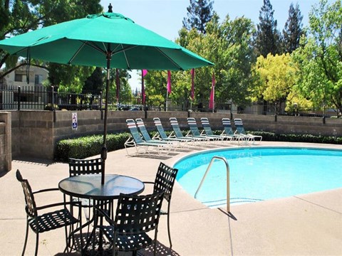 A pool area with a table and chairs and a green umbrella.