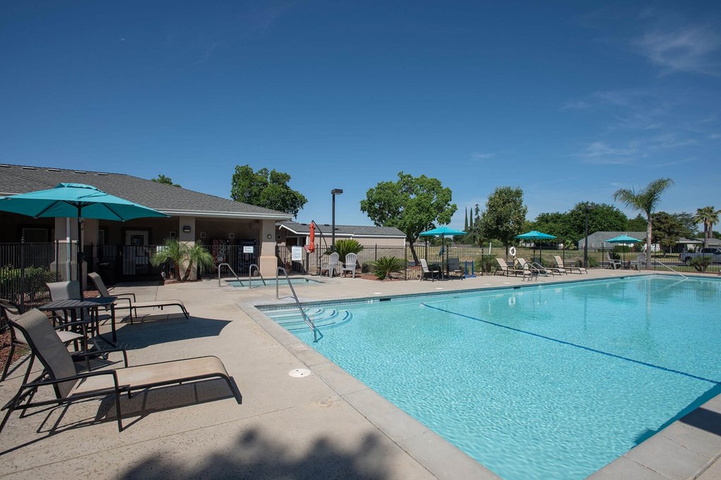 a swimming pool with chairs and umbrellas next to a building at Castle Vista Senior Duplex Community, Atwater, California