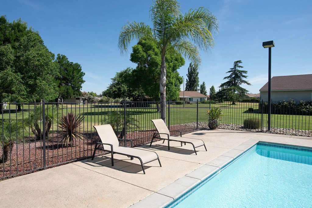 a swimming pool with two lounge chairs next to a fence at Castle Vista Senior Duplex Community, Atwater