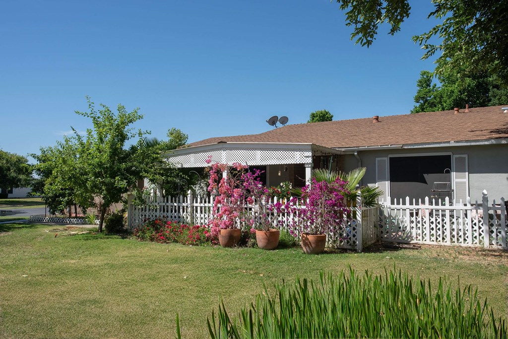 a house with potted flowers in front of a white fence at Castle Vista Senior Duplex Community, Atwater, CA, 95301