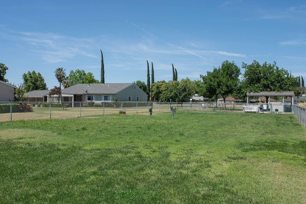 a fenced in dog park with a house in the background at Castle Vista Senior Duplex Community, Atwater, California