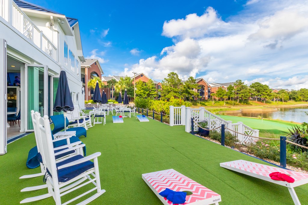 the back patio of a house with chairs and tables on the grass