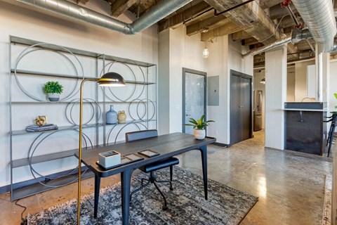 Industrial Style Apartment  with Exposed Ducts and Concrete, Area Rug Under Desk in Front of Contemporary Shelf with Plants and Decorations Next to Kitchen with Breakfast Bar