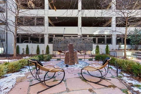 Courtyard Lounge with Stones, Contemporary Rocking Chairs and Contemporary  Round Swings in Front of Decorative Metal Piece in Front of Parking Garage