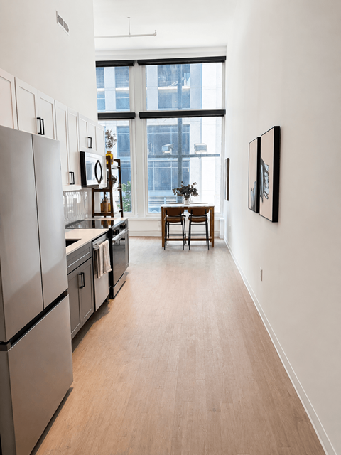 A kitchen with a refrigerator, a dining table and chairs, and a painting on the wall.