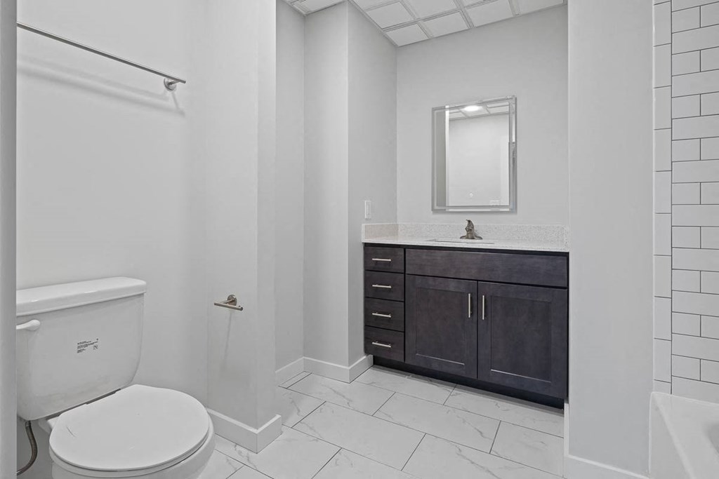 A white toilet is in a bathroom with a white tile floor and a white shower curtain at Hampton Plaza Apartments, Towson, Maryland