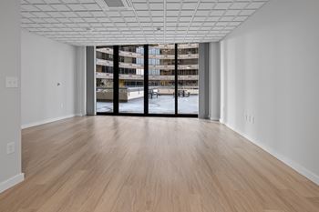 A room with a wooden floor and a large window with a view of a building outside at Hampton Plaza Apartments, Towson, MD, 21286