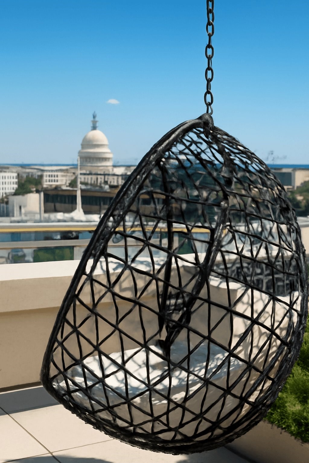 A black hanging chair with a white cushion is suspended from a chain.