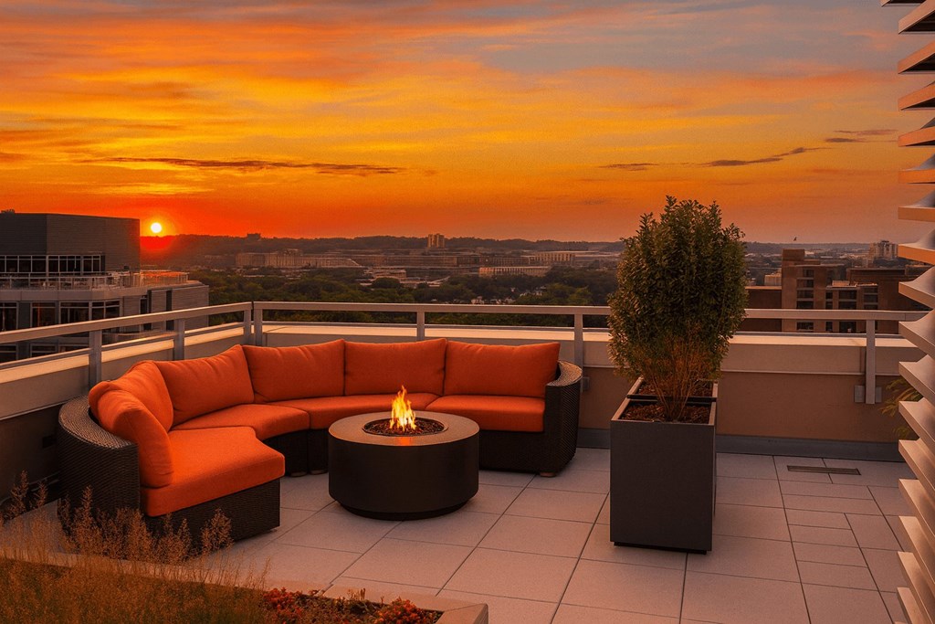 A patio with a fire pit and seating area overlooking a cityscape at sunset.
