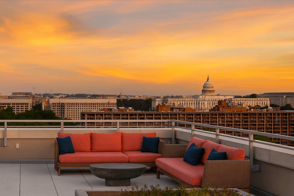 A red couch with blue pillows is on a balcony overlooking the city.