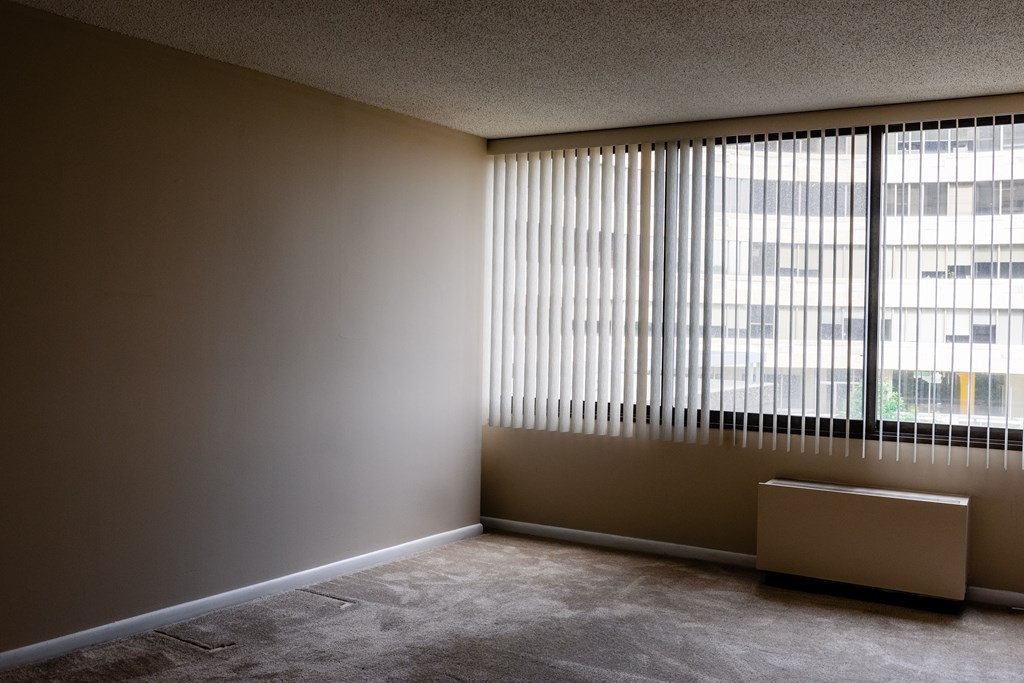 A room with a window covered by blinds and a radiator on the floor at Hampton Plaza Apartments, Maryland