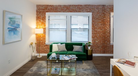A living room with a green couch and a brick wall.