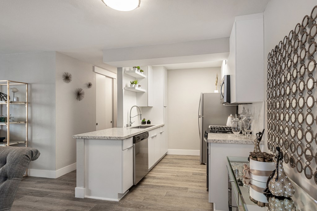Apartments in Hollywood, CA, with In-Unit Washer and Dryer - Candela - Kitchen with Luxury Vinyl Plank Flooring, Customized White Cabinetry, Stainless Steel Appliances, Quartz Countertops, Shelves, Home Decor, and Kitchen Island with Single Sink and Gooseneck Faucet.