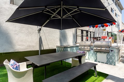 a picnic table with an umbrella and chairs on a backyard patio