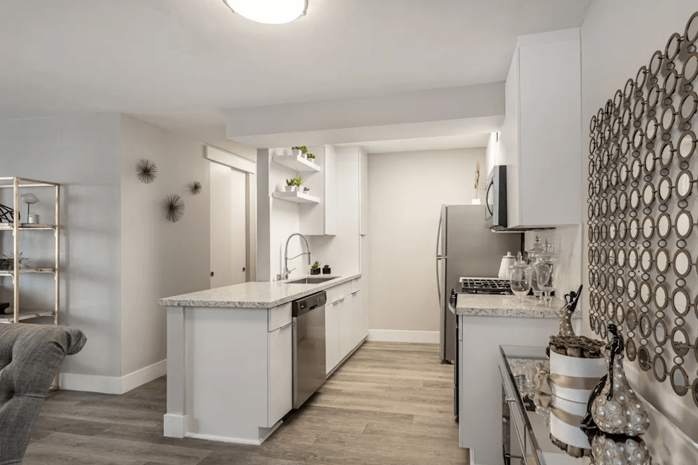 Apartments in Hollywood, CA, with In-Unit Washer and Dryer - Candela - Kitchen with Luxury Vinyl Plank Flooring, Customized White Cabinetry, Stainless Steel Appliances, Quartz Countertops, Shelves, Home Decor, and Kitchen Island with Single Sink and Gooseneck Faucet.