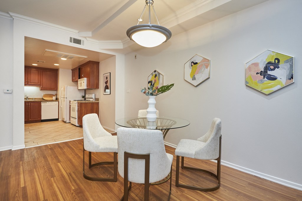 Dining table just outside spacious kitchen with wooden cabinets and white walls