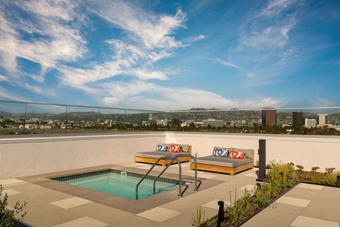 a rooftop terrace with a pool and two chairs and a city in the background
