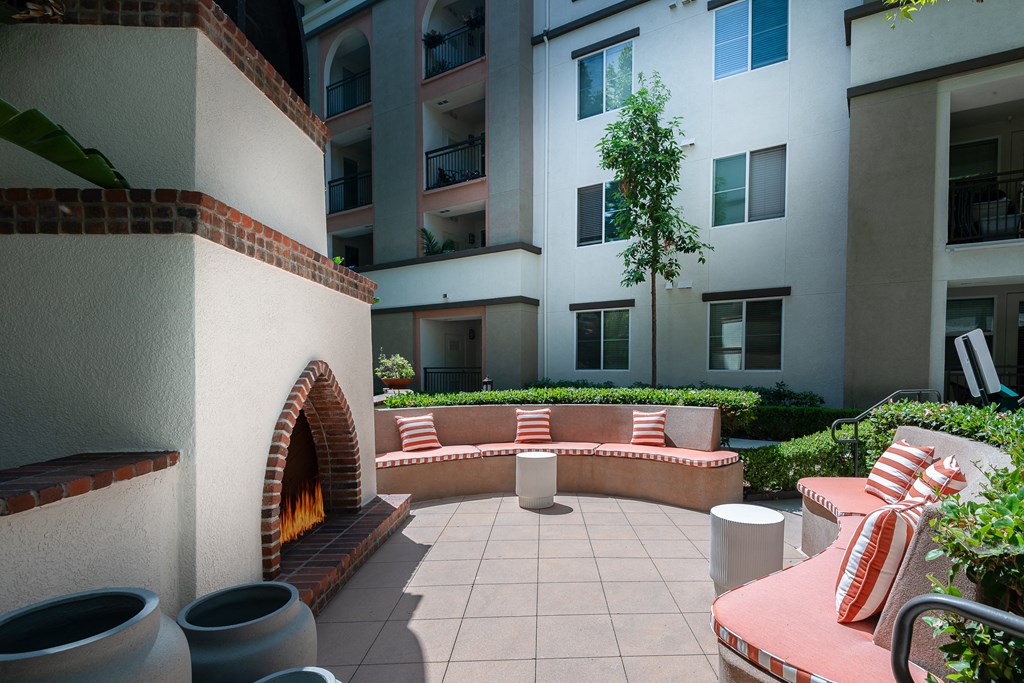 a seating area with a fireplace on a patio with an apartment building in the background