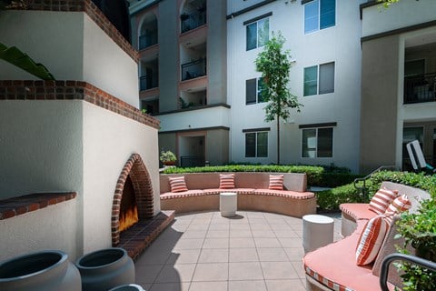a seating area with a fireplace on a patio with an apartment building in the background