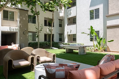 a patio with couches and a ping pong table in front of an apartment building