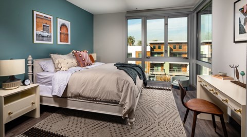 bedroom with large windows and a bed with blankets and pillows