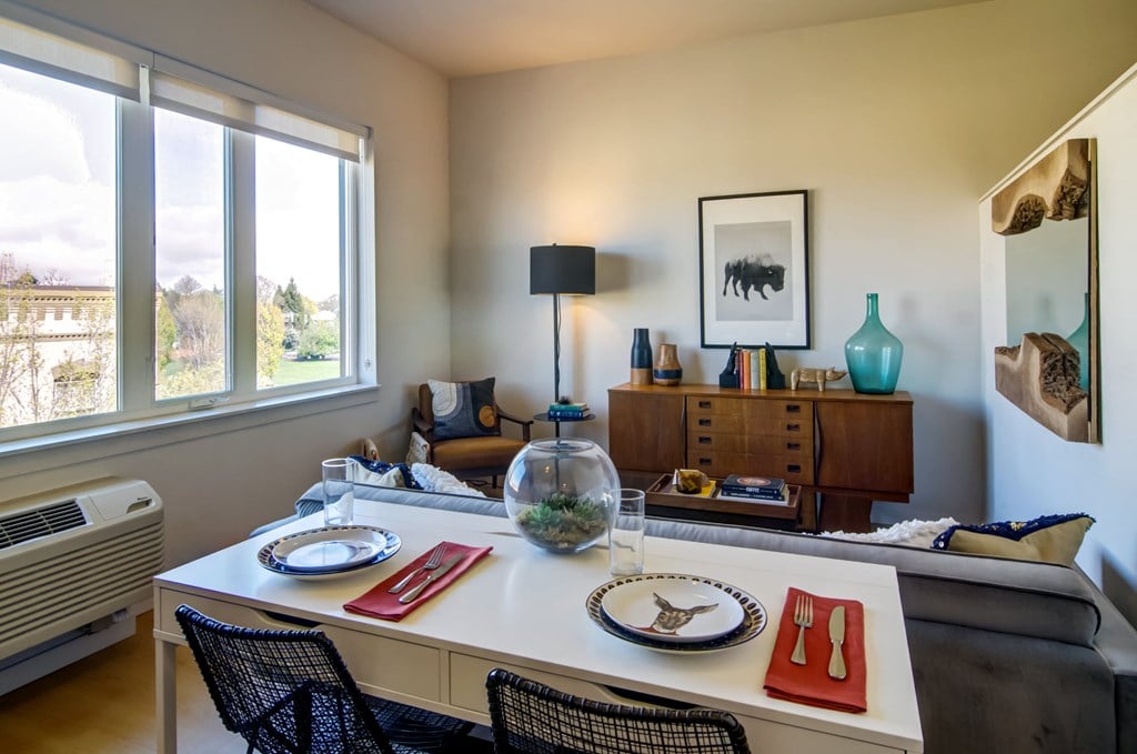 Unit living area with dining table, couch and seating area next to large window