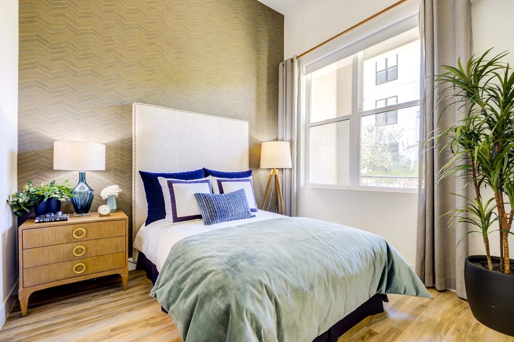 Homey bedroom with full bed and bedside table next to large window and potted tree